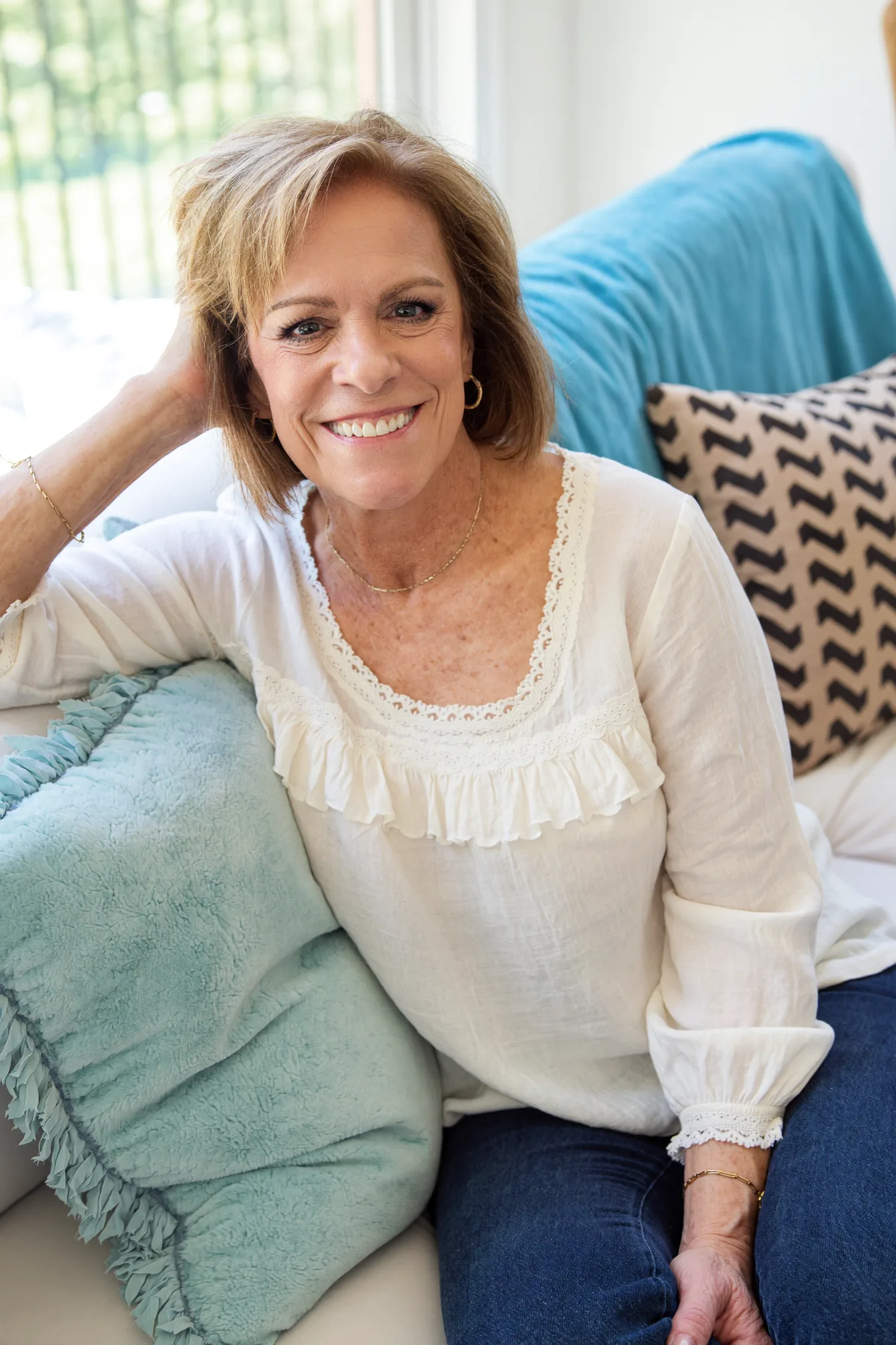 Jill Prescott smiling warmly, relaxing on a sofa with soft blue pillows